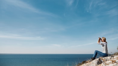 Mulher de binóculos a ver o mar, representa Fundo de Pensões Aberto BPI Valorização da BPI Vida e Pensões.