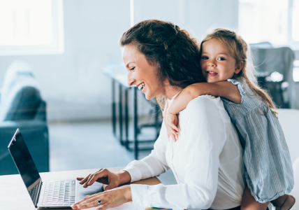 Mãe ao computador com filha às cavalitas. Representa a proteção do Seguro Vida Negócios.