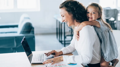 Mãe ao computador com filha às cavalitas. Representa a proteção do Seguro Vida Negócios.